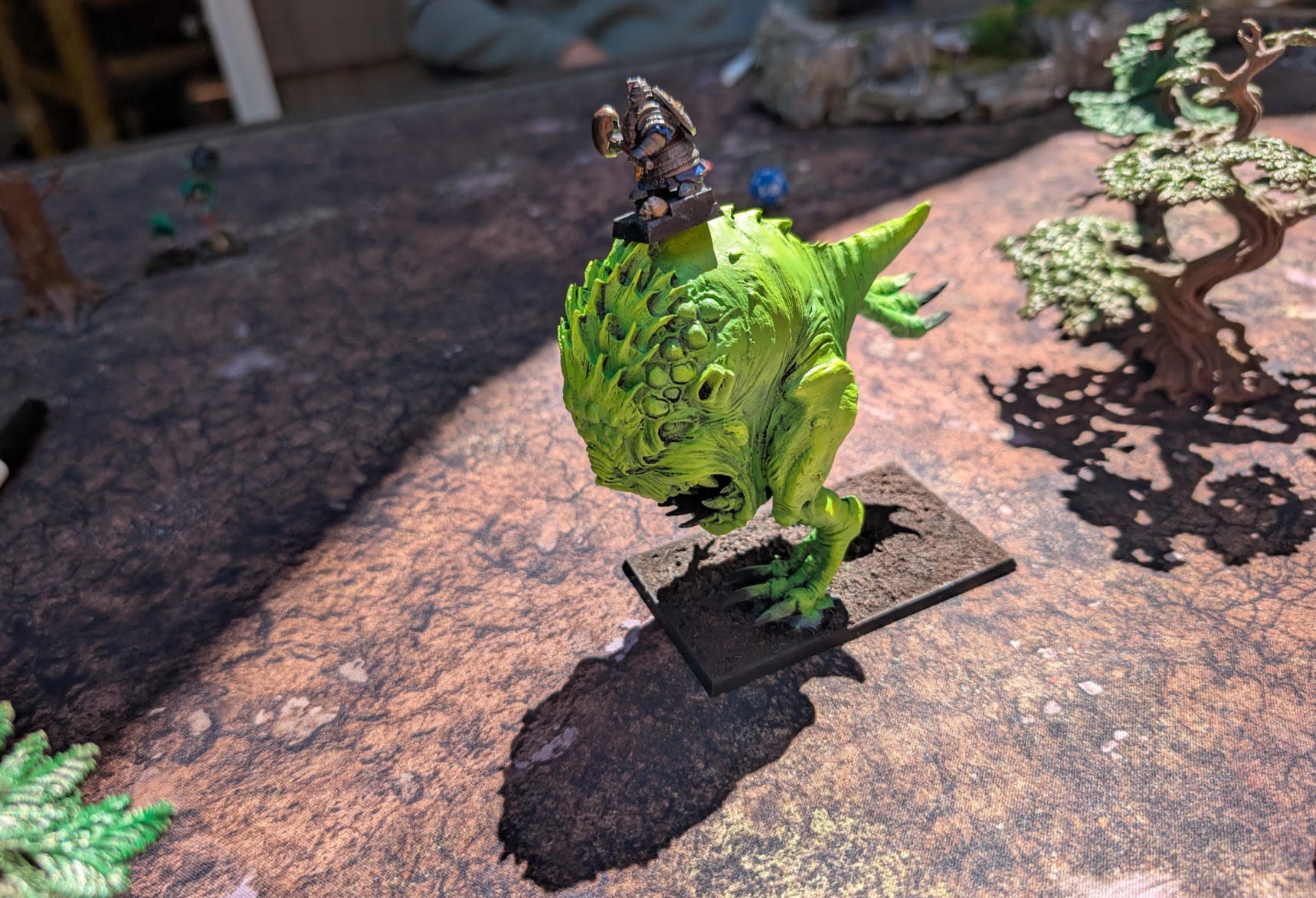 A bright green Colossal Squig miniature bares its teeth, with a small rider perched on its back.